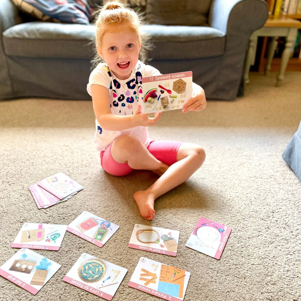 Child holding an activity card from the phase 5 play makes sense phonics activity pack 