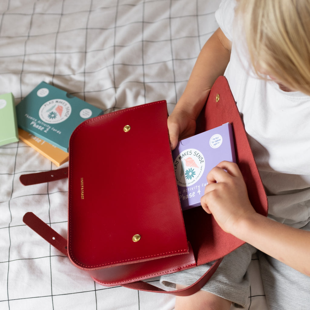 A child putting four packs of Play Makes Sense Phonics Activity Cards into his school bag.