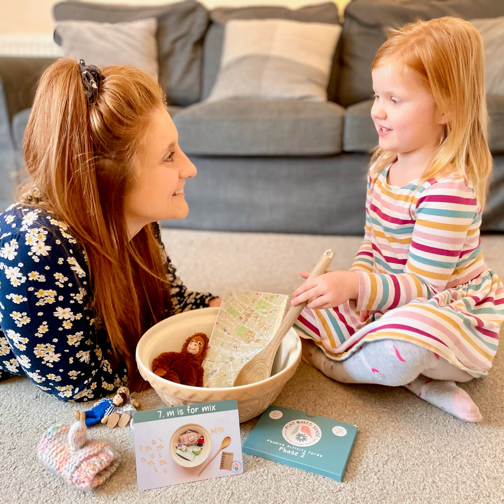a mother and child sat playing together. They look happy. Next to them in a pack of Phase 2 Phonics Cards