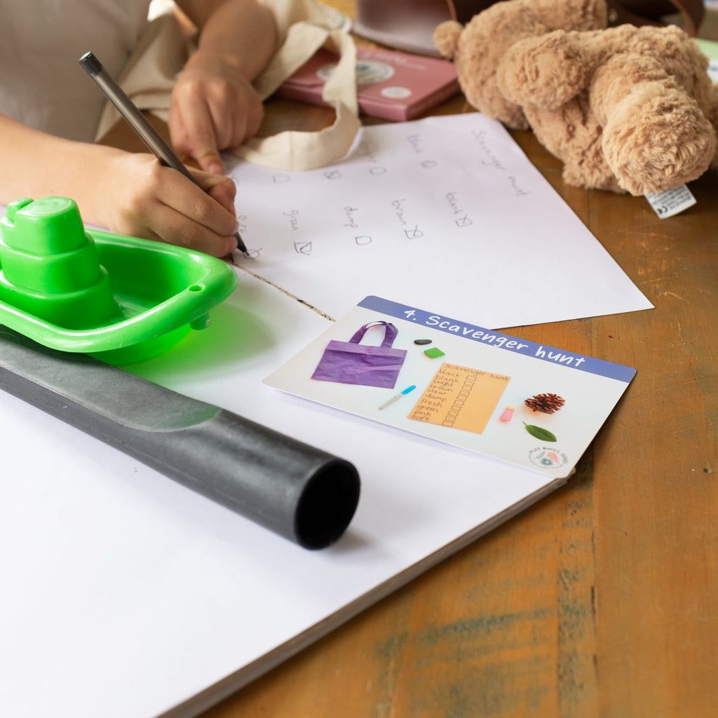 A child writing on a desk. On the desk is a Phonics Phase 4 activity card, a toy boat and a teddy bear.